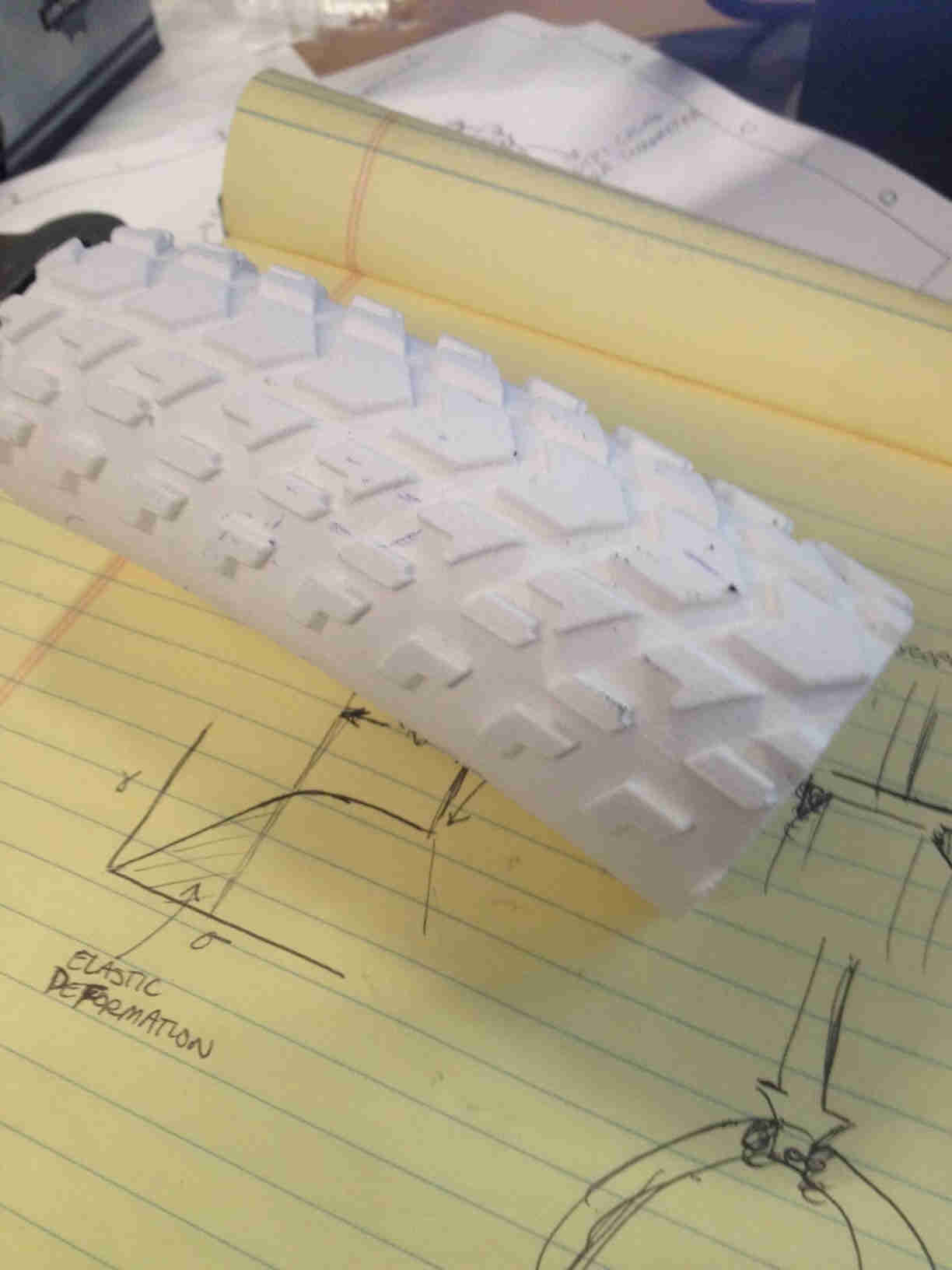 Downward view of a white bike tire cut-out, with the tread facing up, laying across a yellow legal pad - 2nd