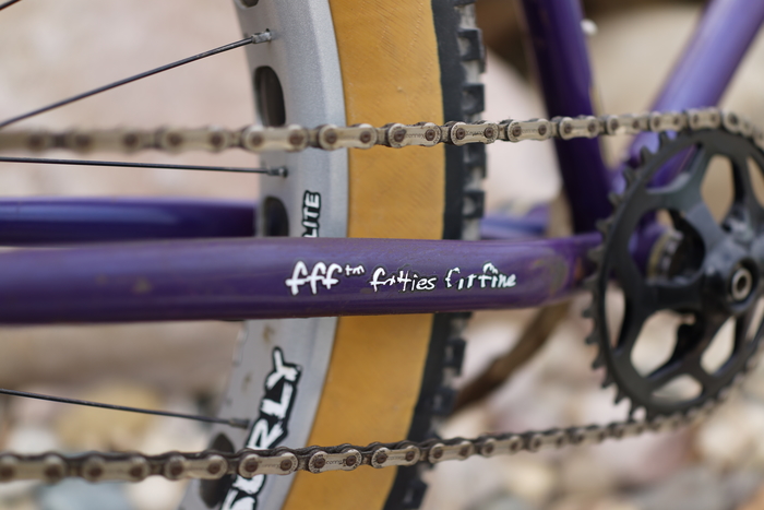 Right side, angled close up of zoom in of a fat bike tire, chain and crankset on a purple Surly Pugsley fat bike