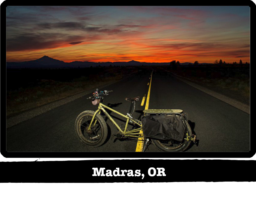 Left side view of Surly Big Fat Dummy bike, green, standing across a highway at sunrise - Madras, OR tag below image