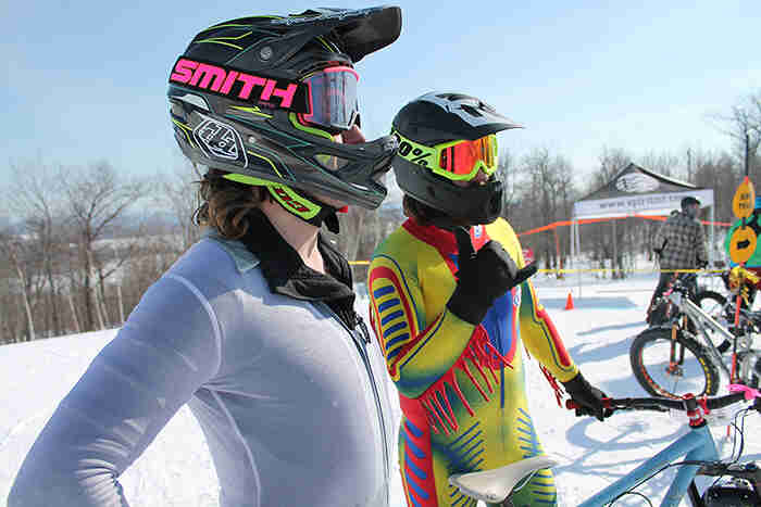 Right profile view of two cyclists wearing helmets and bike race suit, at the bottom of a ski hill