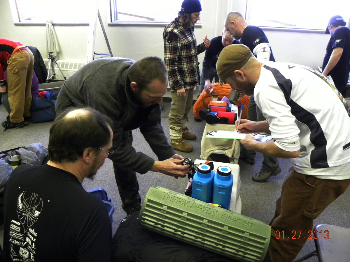 Side view of a group of people sorting through camping gear inside of a room