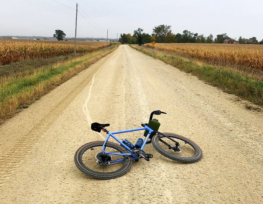 Surly Midnight Special colored in Perry Winkle's Sparkle lying on left side on gravel road between corn fields