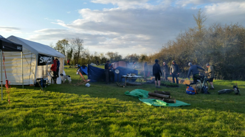 People standing around a campground in a grass field, with a Surly canopy next to them