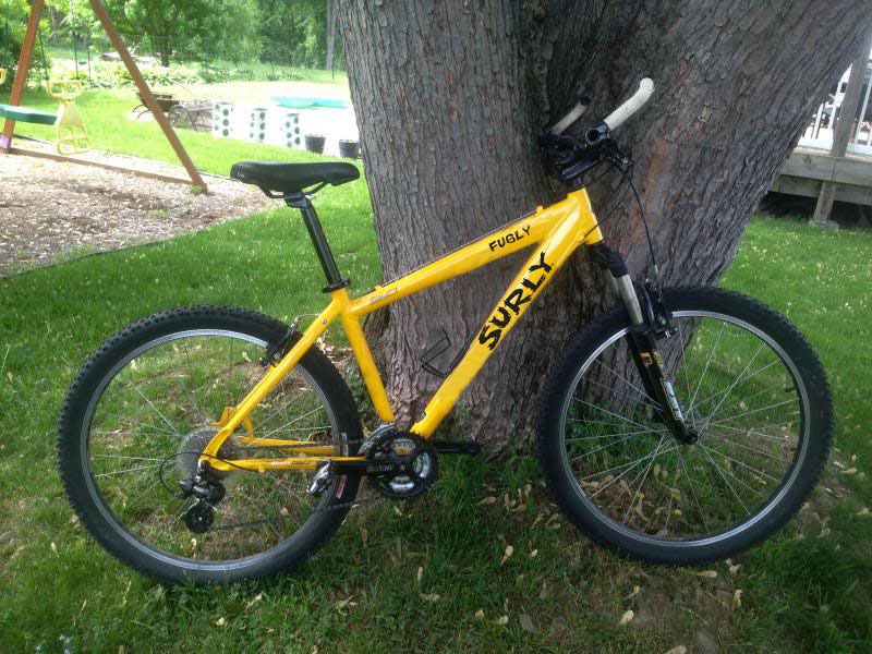 Right side view of a yellow full suspension bike, parked in front of a tree, at a park