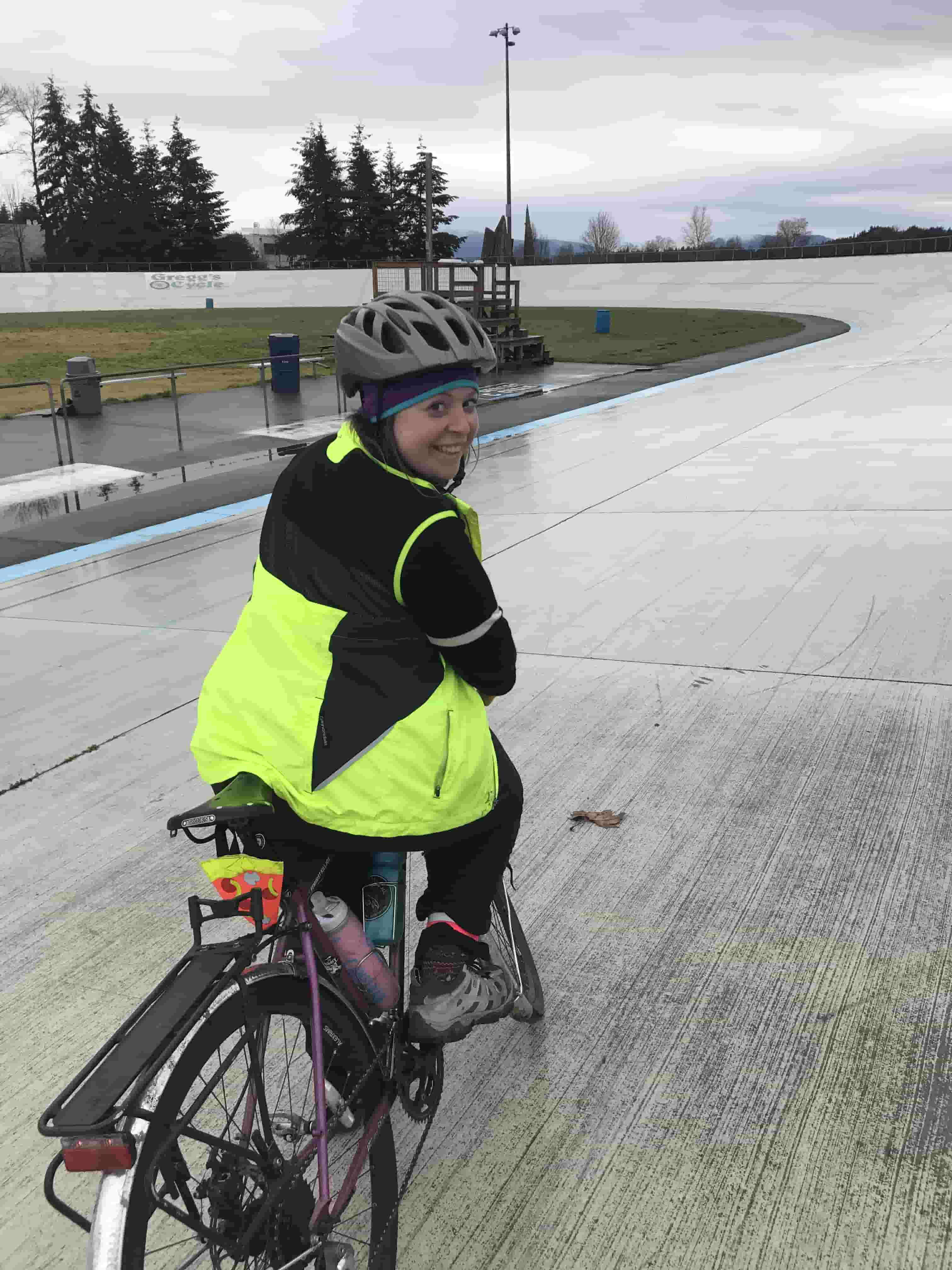Cyclist looking back while seated on a bike in the middle of a race track wearing biking gear on a rainy day