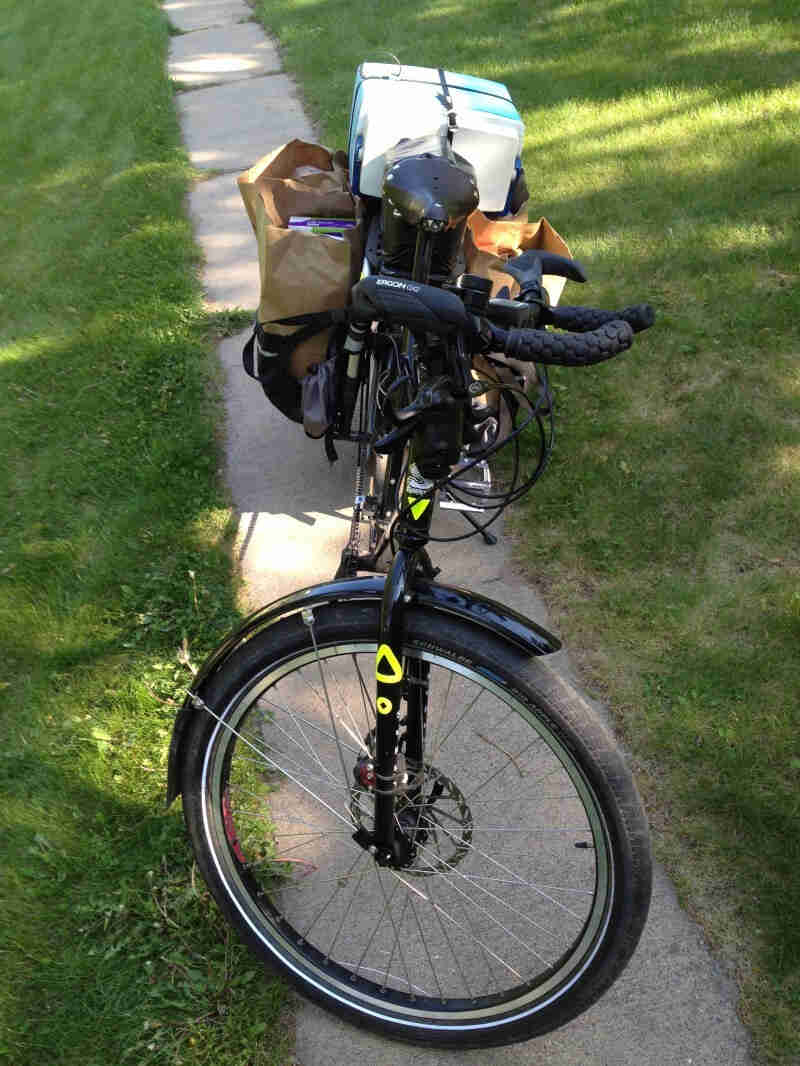 Front view of a black Surly Big Dummy bike hauling groceries, parked on a narrow sidewalk with grass on each side