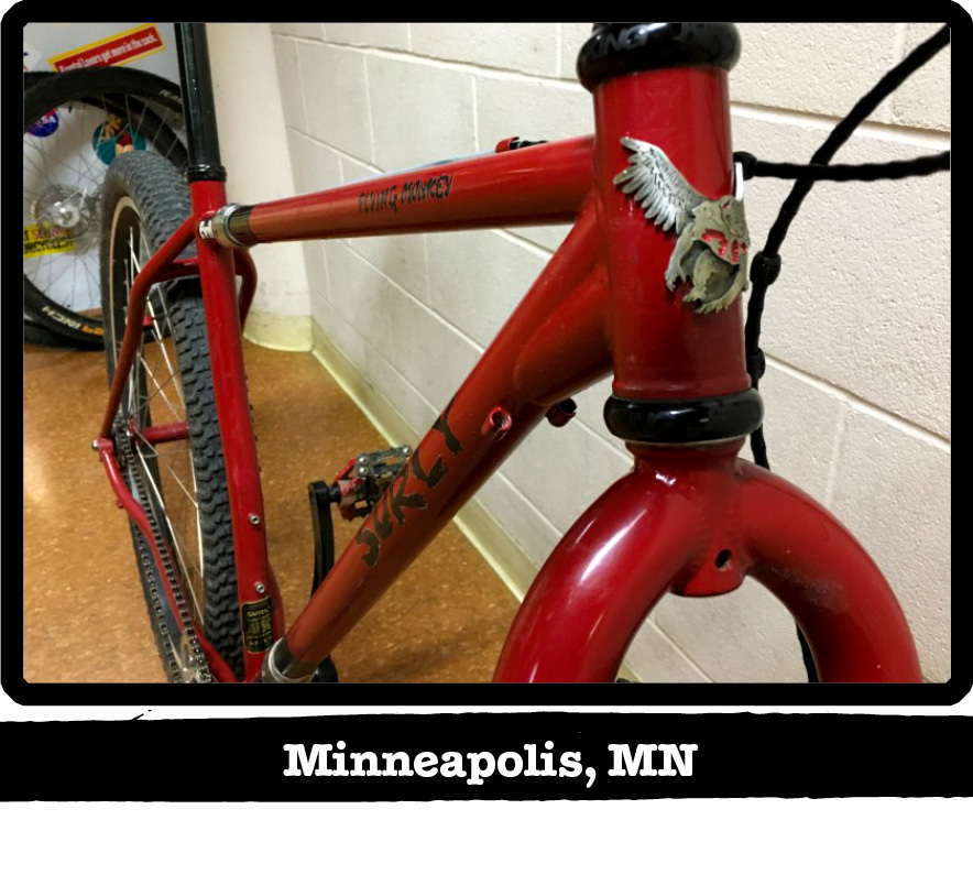 Front view of a red Surly Flying Monkey bike leaning a white cinder block wall-Minneapolis, MN banner below image