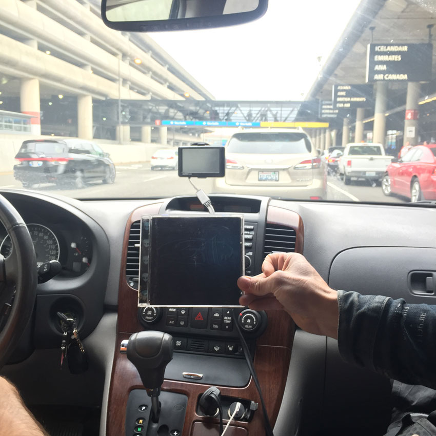 View of a the dashboard area of a vehicle, with a hand holding up a CD case, and traffic seen through the windshield