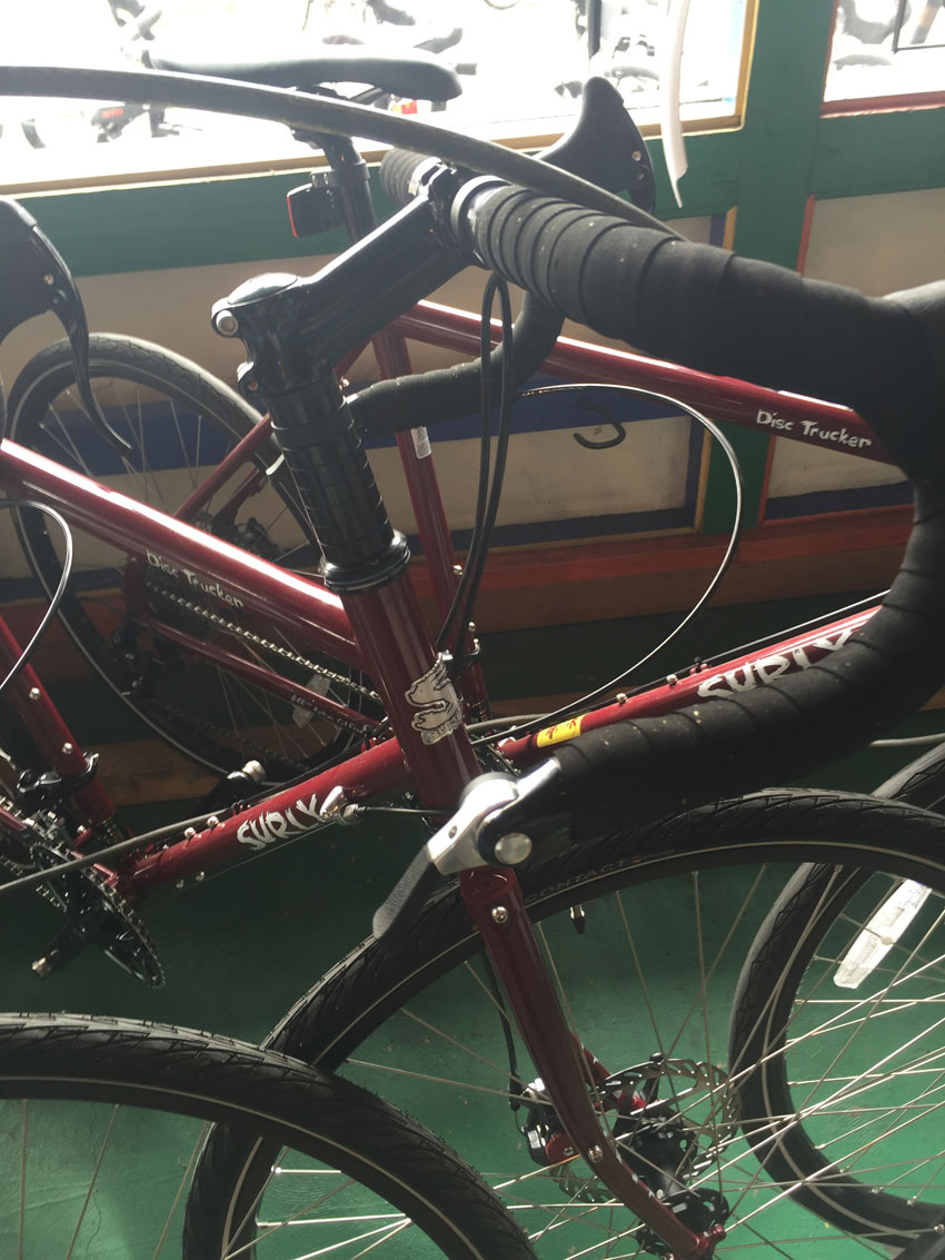 Downward cropped view of 2, red, Surly Disc Trucker bike, on a green floor