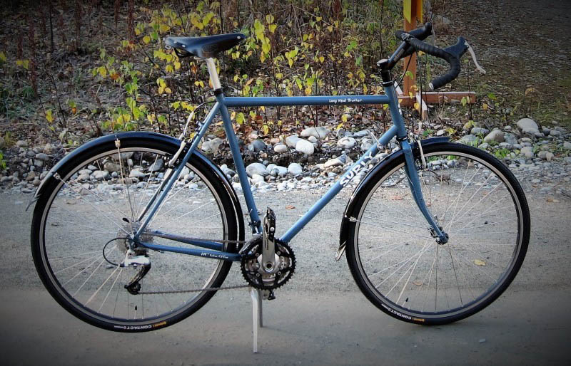 Right side view of a blue Surly Long Haul Trucker bike, parked on a gravel road