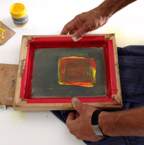 Downward view of a two hands holding a silkscreen frame over a blue shirt