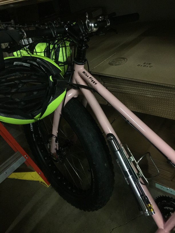 Downward, cropped view of a pink Surly fat bike, next to a stack of cardboard boxes