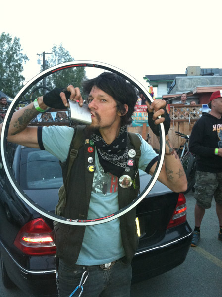 Front view of a person holding and looking through a bike rim, and drinking from a flask