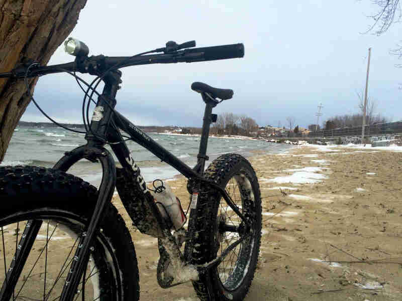 Front, left side view of a black Surly Ice Cream Truck fat bike, parked on a frozen sand lake shore