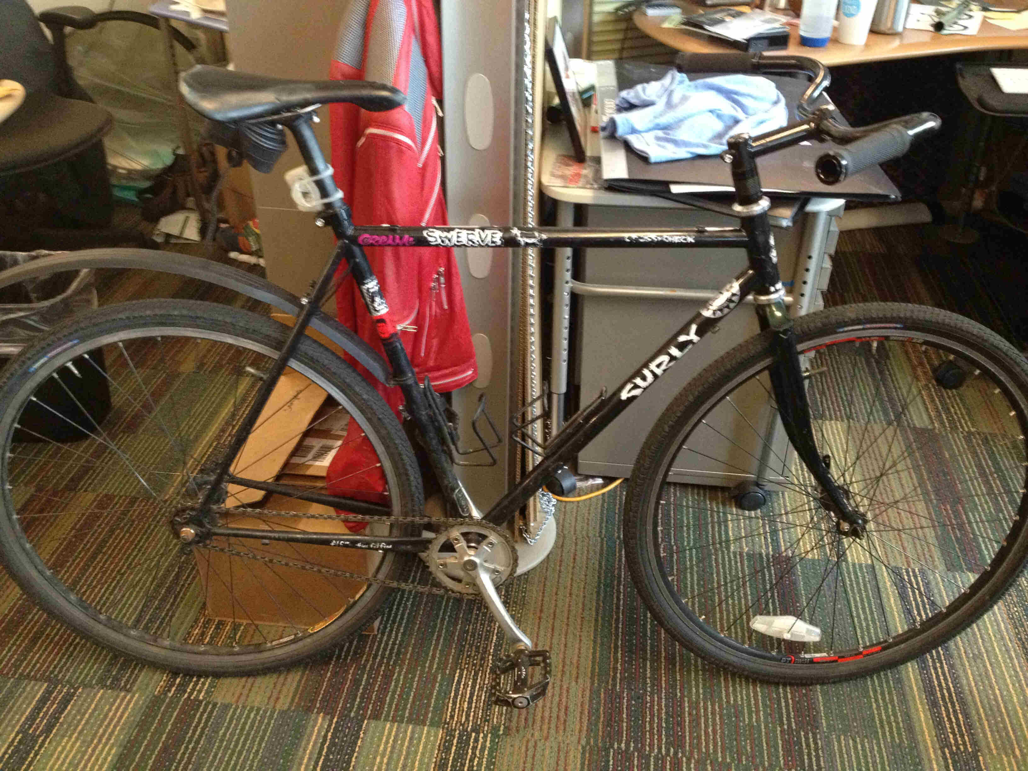 Right side view of a black Surly Cross Check bike, leaning on the end of a cubicle wall, in an office