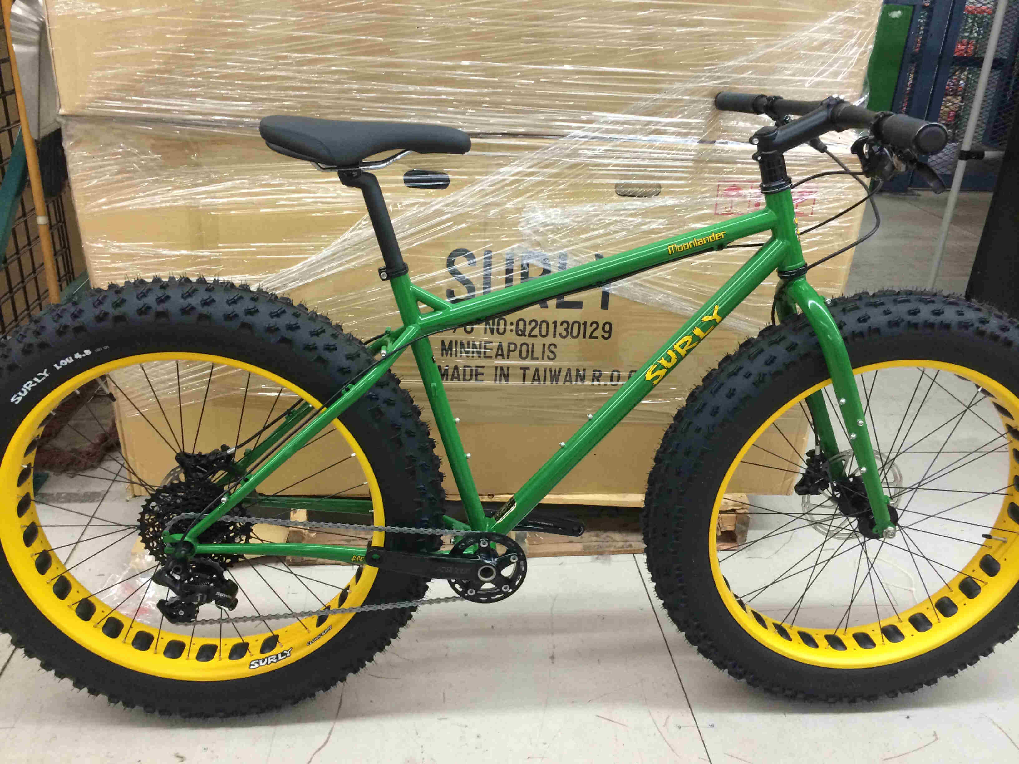 Right side view green Surly Moonlander fat bike, parked against a pallet of cardboard boxes, on a concrete floor