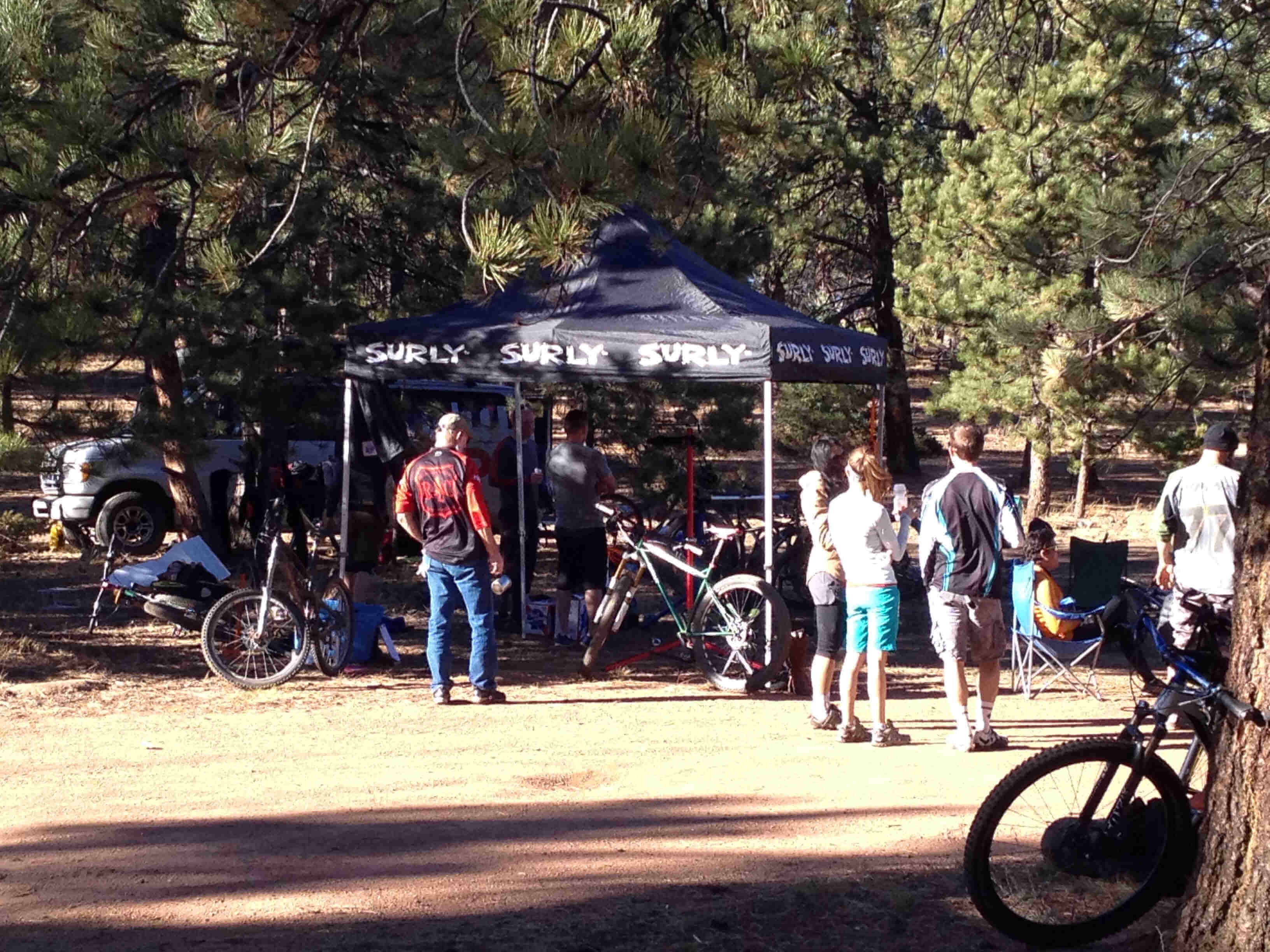 Rear view of people standing in front of a Surly Bikes canopy, with bikes parked around, on a clearing in a forest