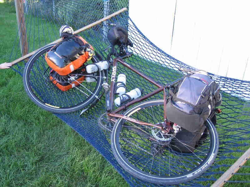 Downward, left side view of a brown Surly bike, loaded with gear and laying in a hammock, on a green grass yard