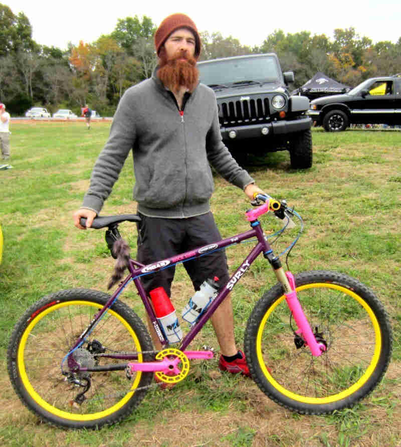 Right side view of a purple Surly Troll bike, with a cyclist standing on the left side in a grass field