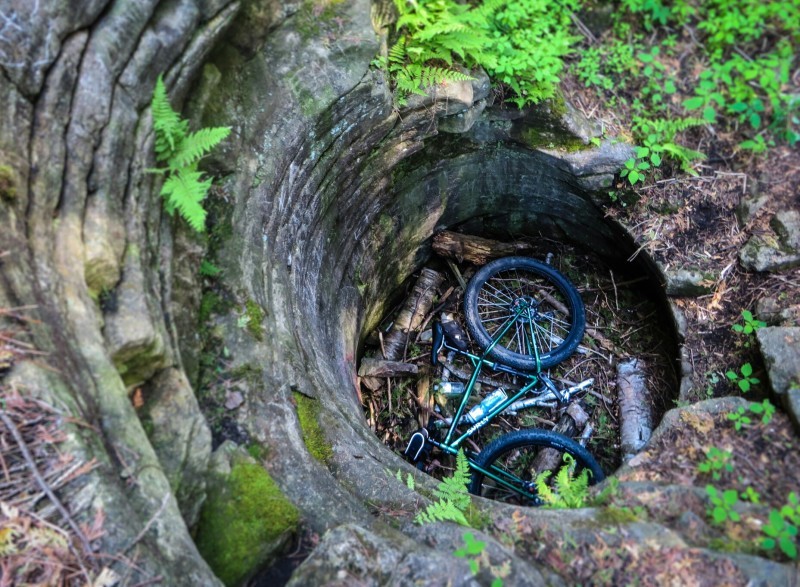 Downward view of a green Surly Krampus bike, laying at the bottom of a stone silo in the woods