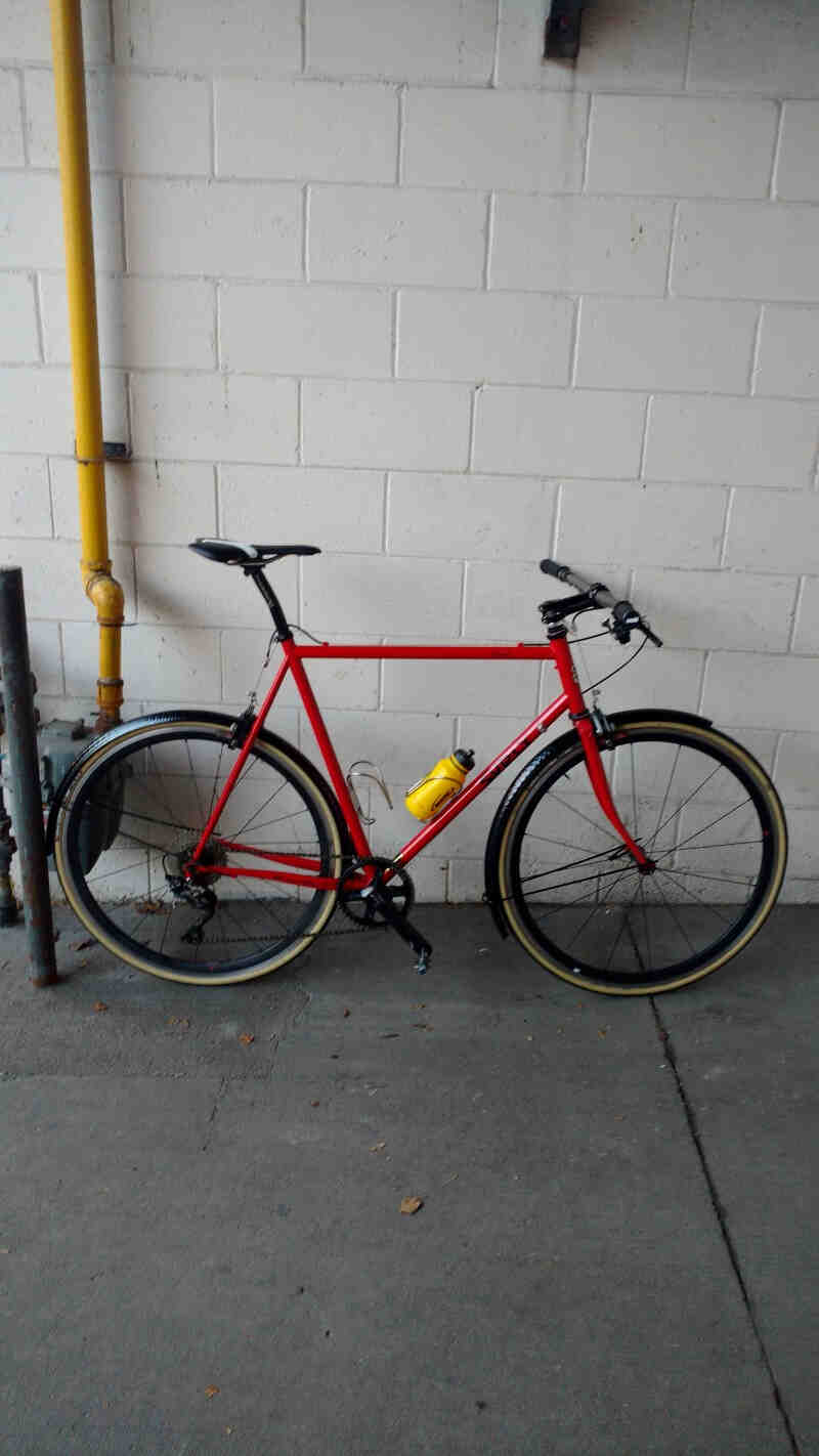Ride side view of a Surly Pacer bike, red, on a sidewalk leaning on a white cinder block wall