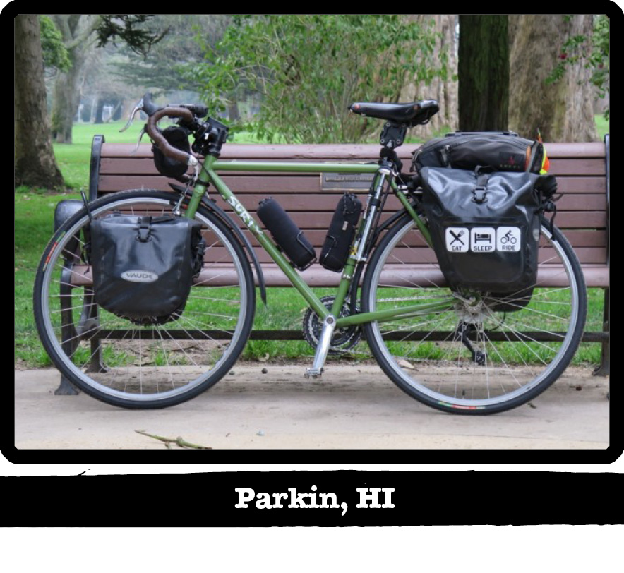 Left profile of a green Surly bike with gear, leaning on a park bench with trees behind-Parkin, HI banner under image