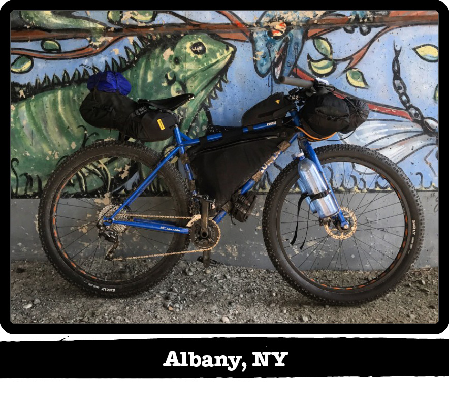 Right profile view of a blue Surly bike with gear leaning on wall with a painting-Albany, NY banner under image