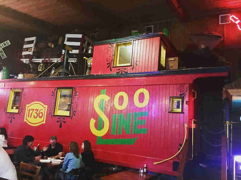 A red Soo Line rail car in a restaurant with people sitting at a table in front of it 