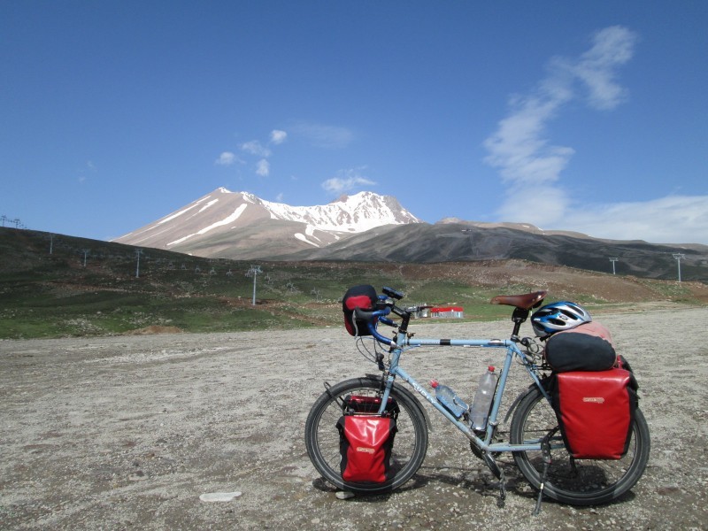 Left side view of a light blue Surly bike, loaded with gear, parked on a rocky field, with mountains in the background