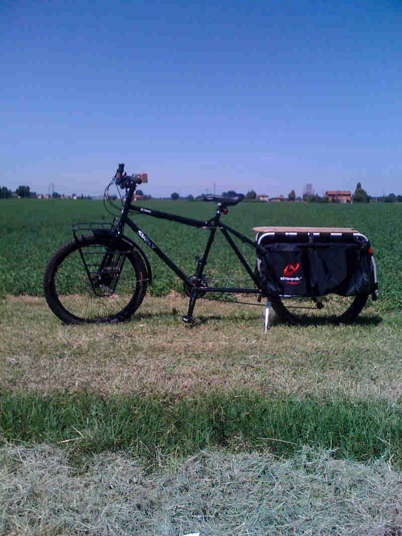 A Surly Big Dummy bike, black, parked in grass in front of a green field - left profile view