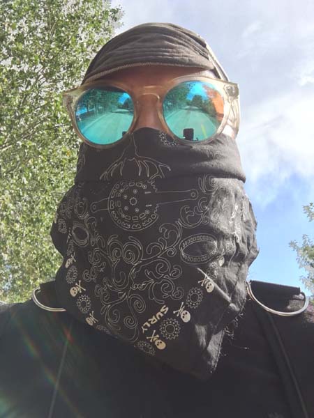 Front view of a person wearing a cap, sunglasses, and a black Surly bandana covering their face