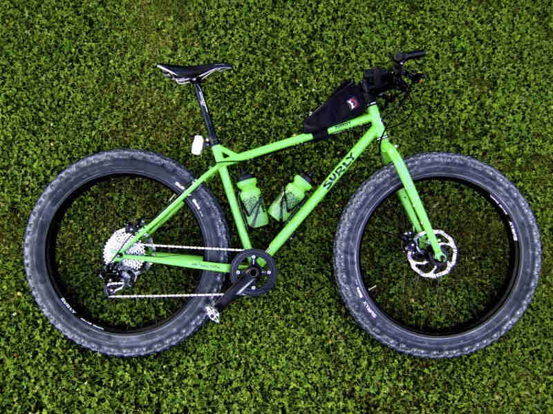 Downward, right side view of a lime Surly Pugsley fat bike, laying on it's left side in short, green grass