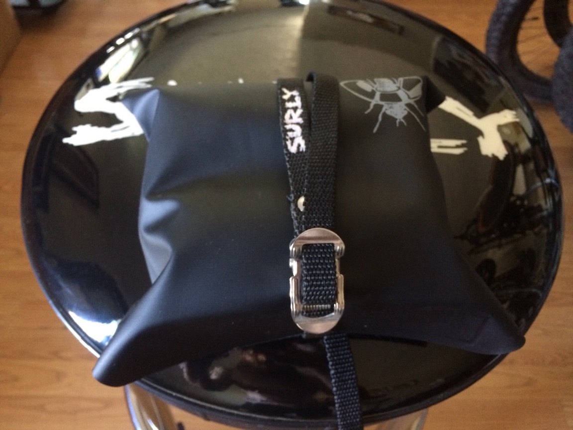 A Surly tool bag, black, packed with gear, with a strap wrapped around it, on top of a barstool seat