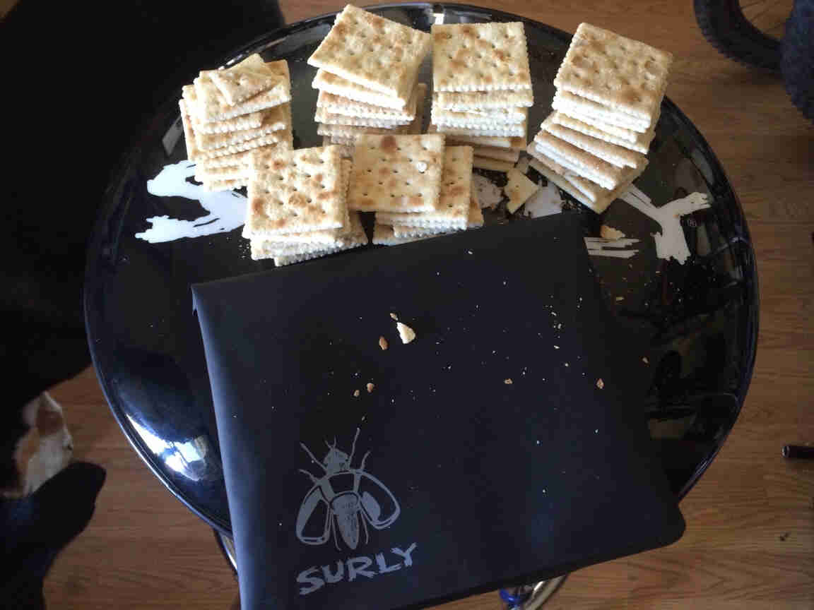 A Surly tool bag, black, with stacks of saltine crackers, on top of a barstool seat