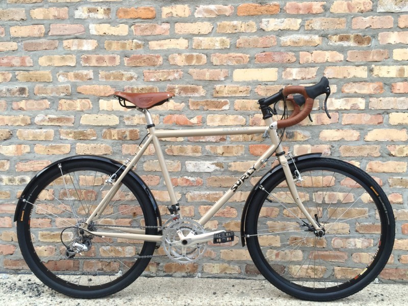 Right side view of a tan Surly Long Haul Trucker, leaning against a brick wall