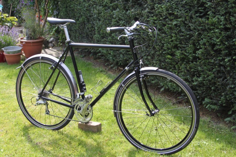 Right side view of a black Surly bike with fenders, parked in a grass yard, next to hedge bushes