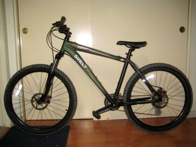 Left side view of an olive Surly bike, parked against white closet doors in a room