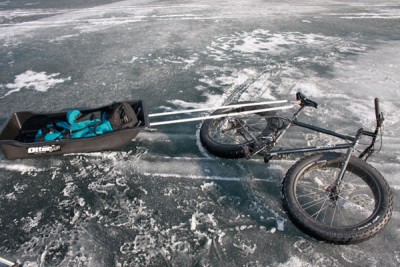 Right side view of a black Surly Moonlander fat bike, laying on it's side with a trailer sled attached, on an icy area