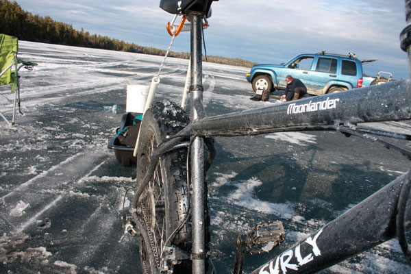 Front, right side view of a Surly Moonlander fat bike with a trailer sled behind it, standing on a frozen lake