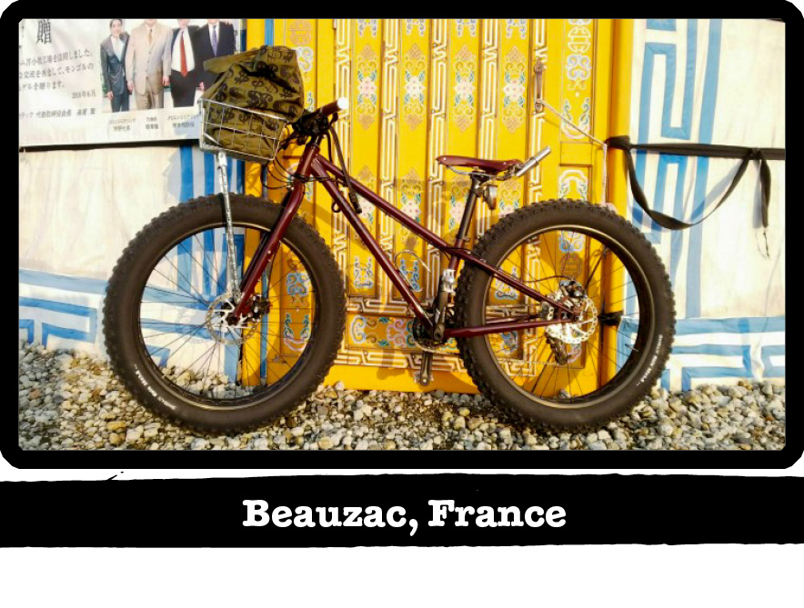 Left profile of a dark red Surly fat bike leaning a colorful wall on gravel-Beauzac, France banner below image
