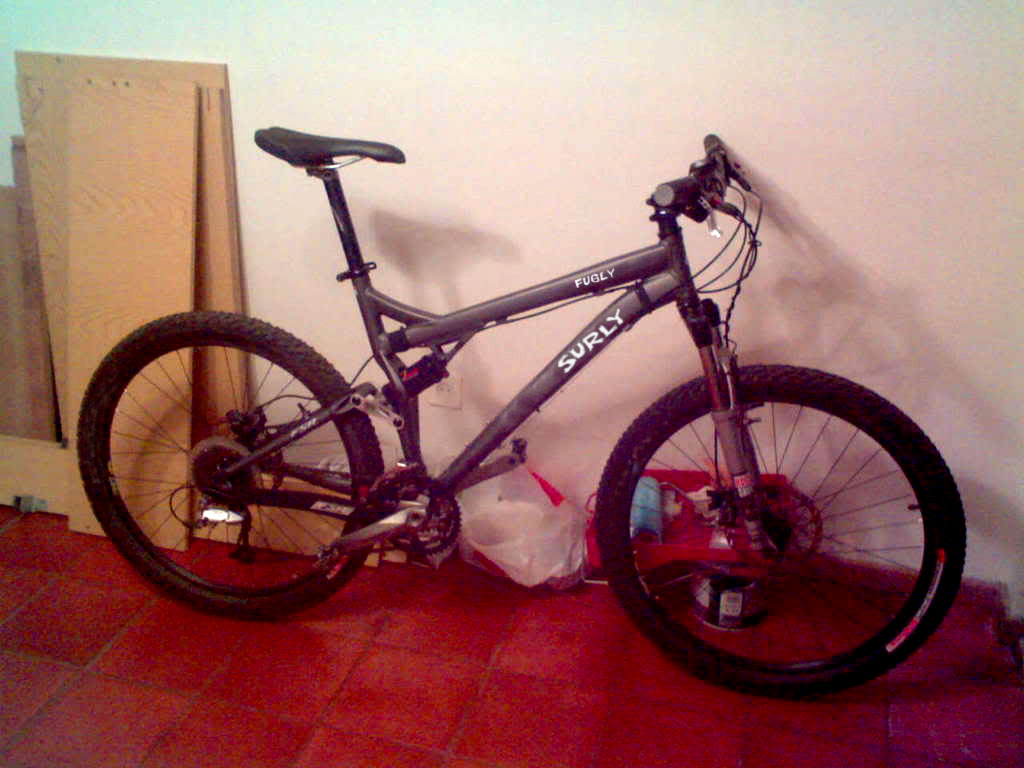 Right side view of a gray full suspension bike, parked along a wall on red tile