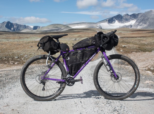 right side view of a purple Surly bike loaded with gear on a gravel road in the mountains