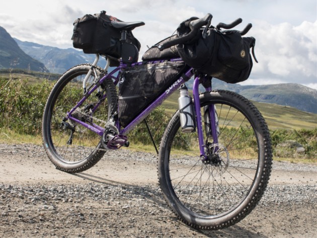 Front view of purple Surly bike loaded with gear standing across a gravel road in the mountains