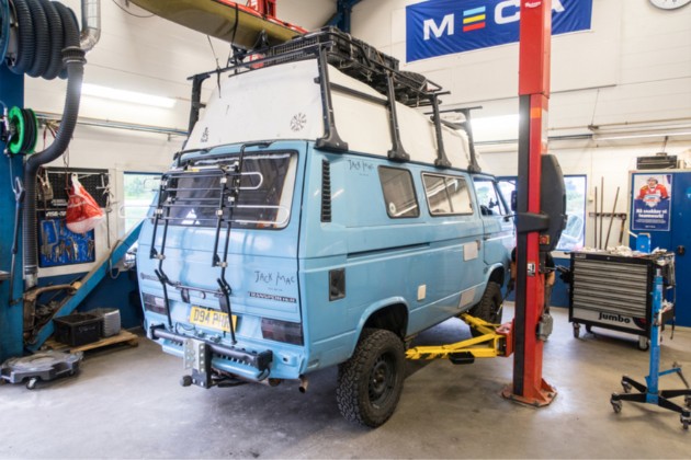Right angled view of a light blue VW van on a car lift in a auto repair shop