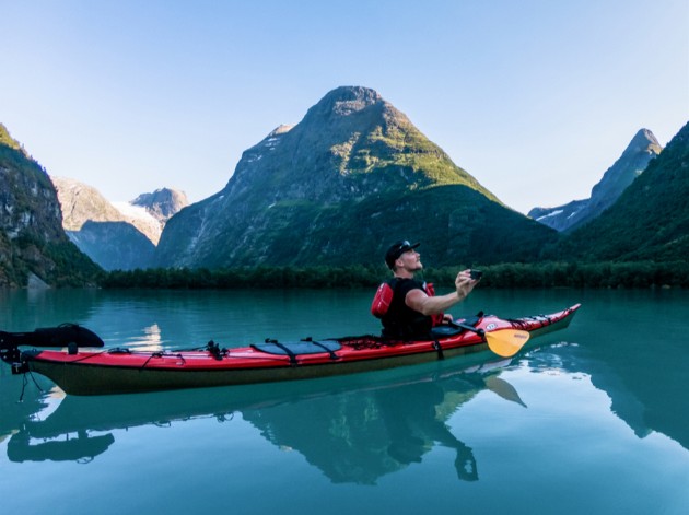 Right side view of a person in a red kayak, on a calm lake in the mountains