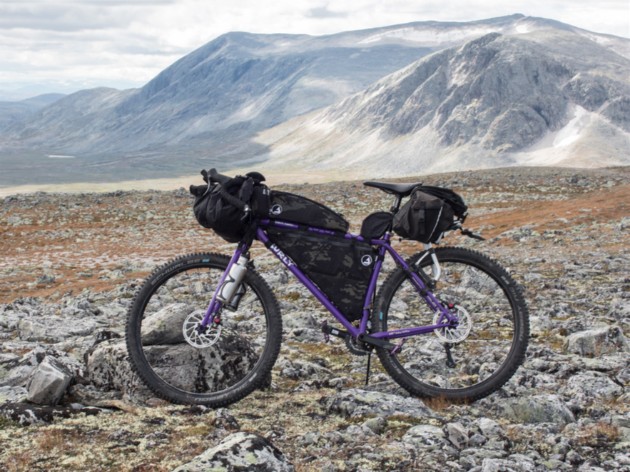 Left side view of a purple Surly bike loaded with gear standing a rocky field in the mountains