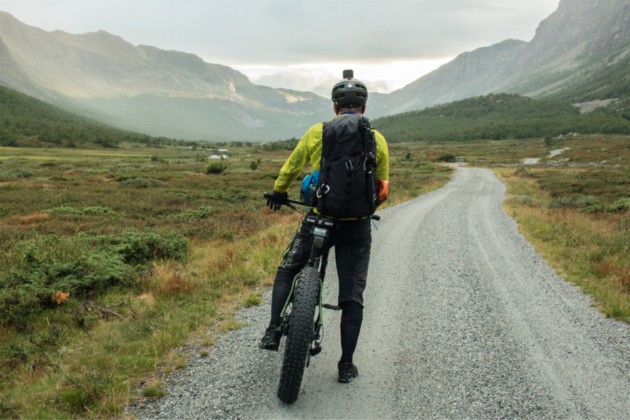 Cyclist facing down a gravel road in the mountains on a fat bike loaded with gear