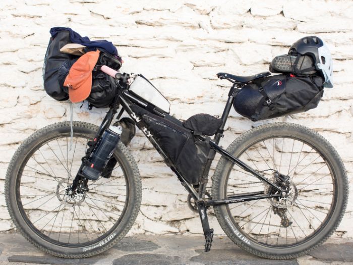 Left side view of a Surly bike loaded with gear leaning against a stone wall 