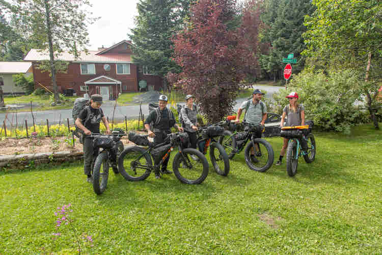 A group of cyclists with their fat bikes loaded with gear, stand on the grass in a front yard