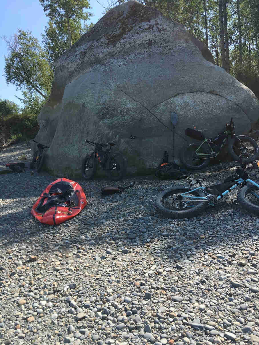 Fat bikes leaning on and around a large boulder on a rocky beach, with tree in the background